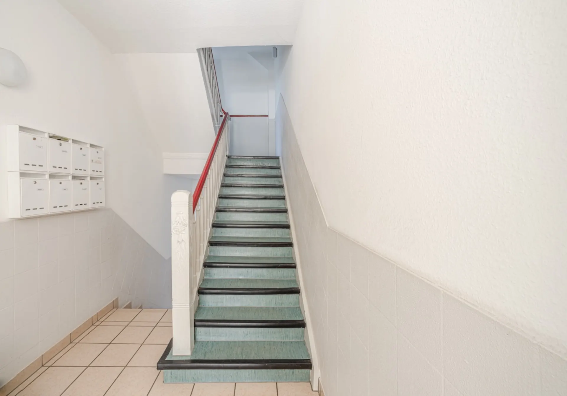 Helles Treppenhaus mit mehreren weißen Briefkästen an der Wand.
