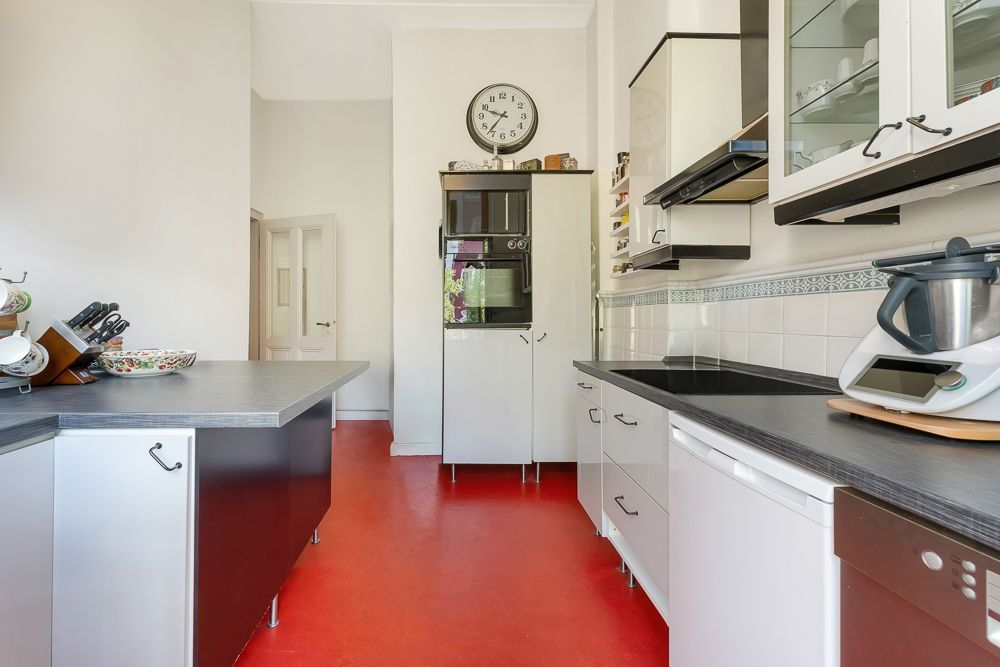 Moderne Küche mit rotem Boden, weißen Schränken und schwarzen Arbeitsplatten.