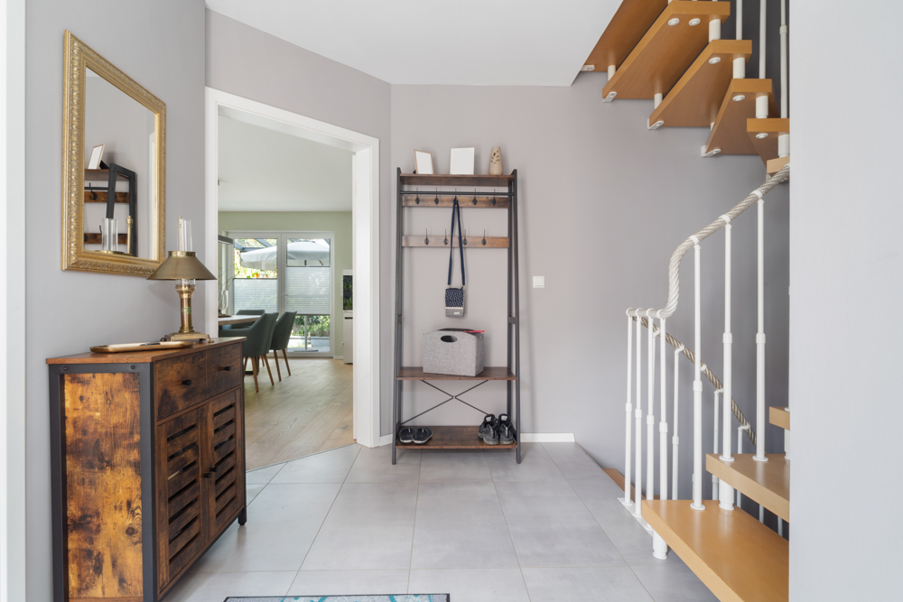 Heller Flur mit Holztreppe, Spiegel, Kommode und Garderobe, Blick ins Esszimmer.
