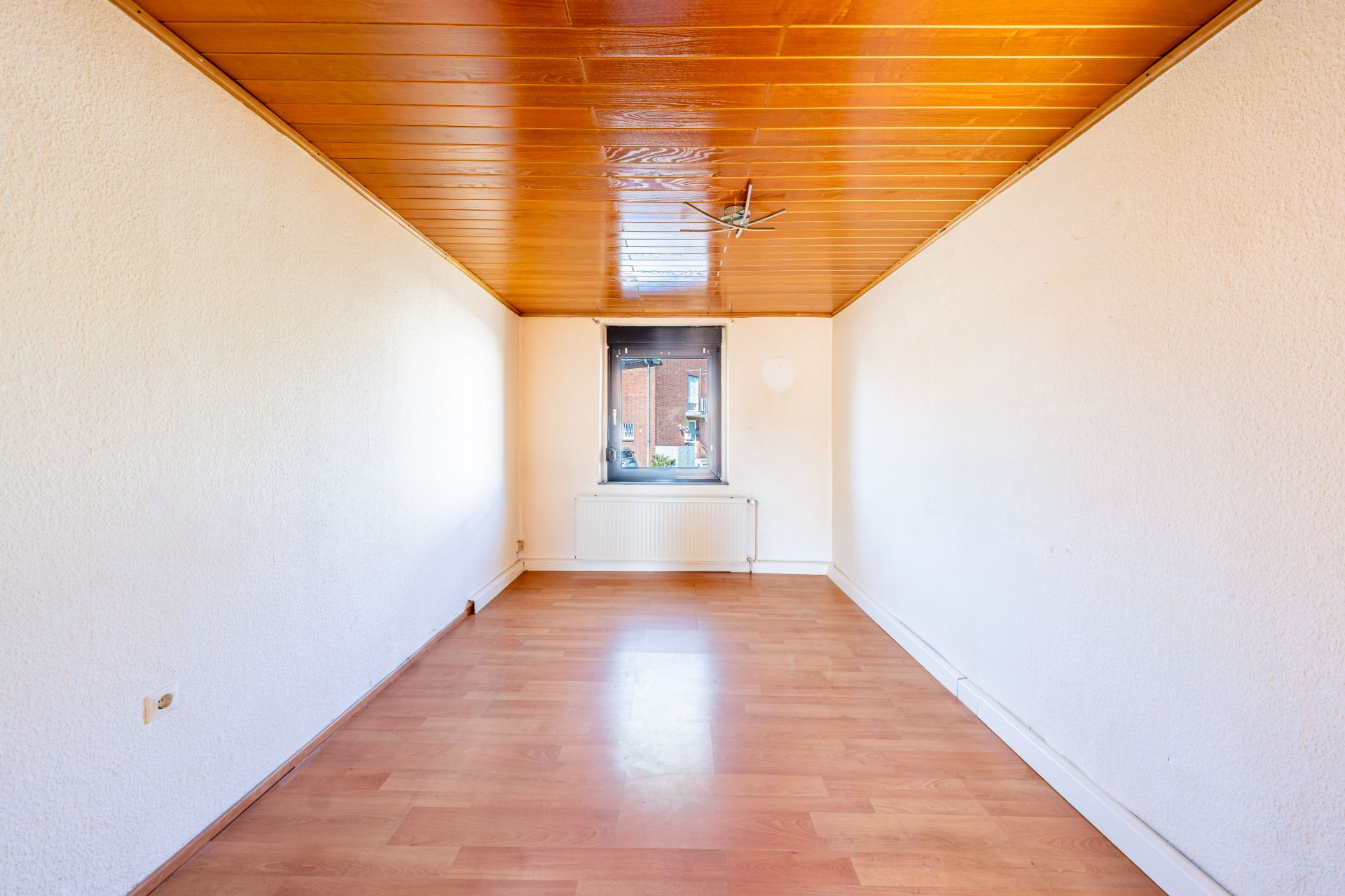 Leerer Raum mit Holzdecke, hellem Boden und Fenster an der Stirnseite.