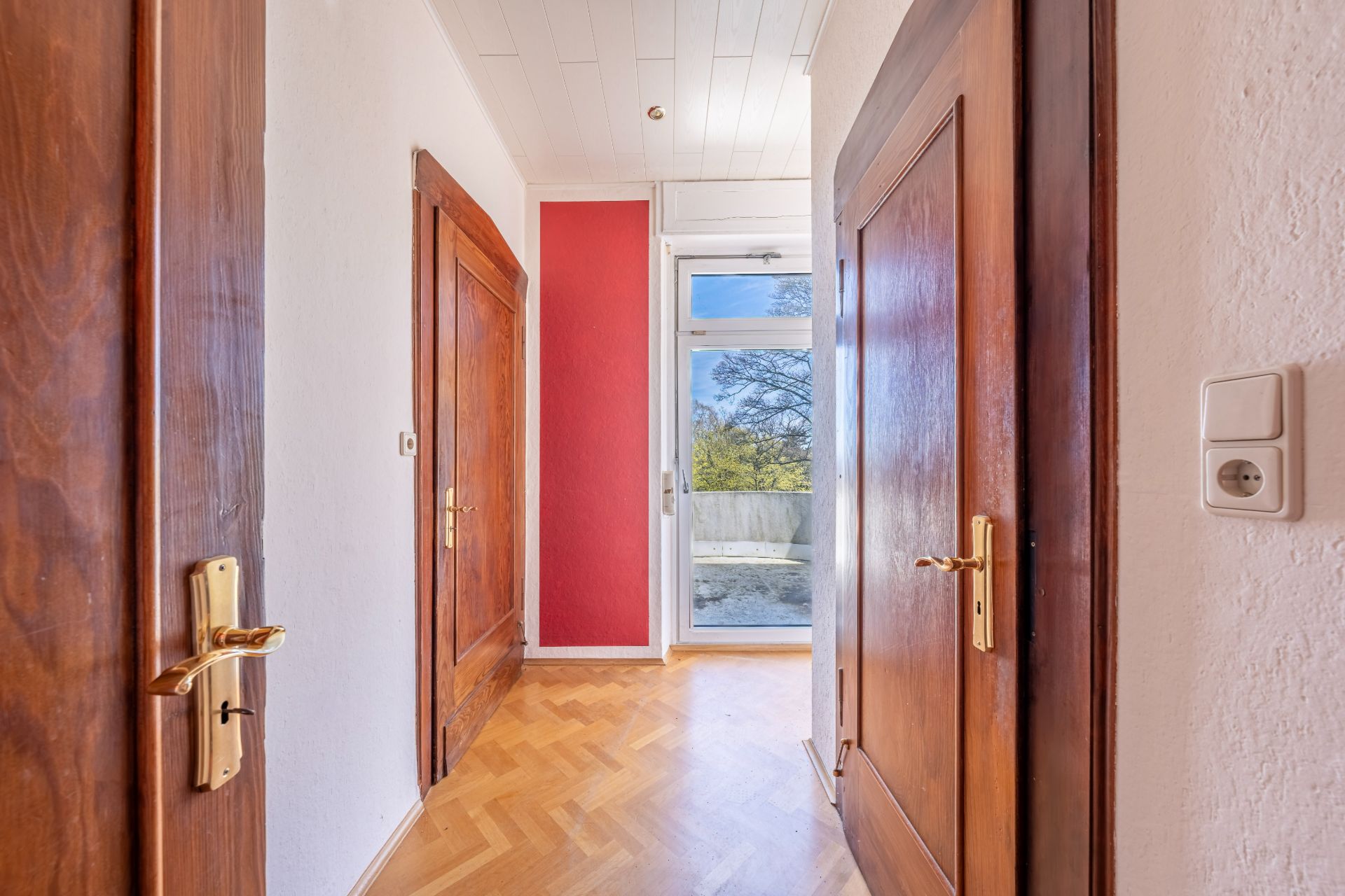Heller Flur mit Parkettboden, Holztüren und Glastür zu einem Balkon.
