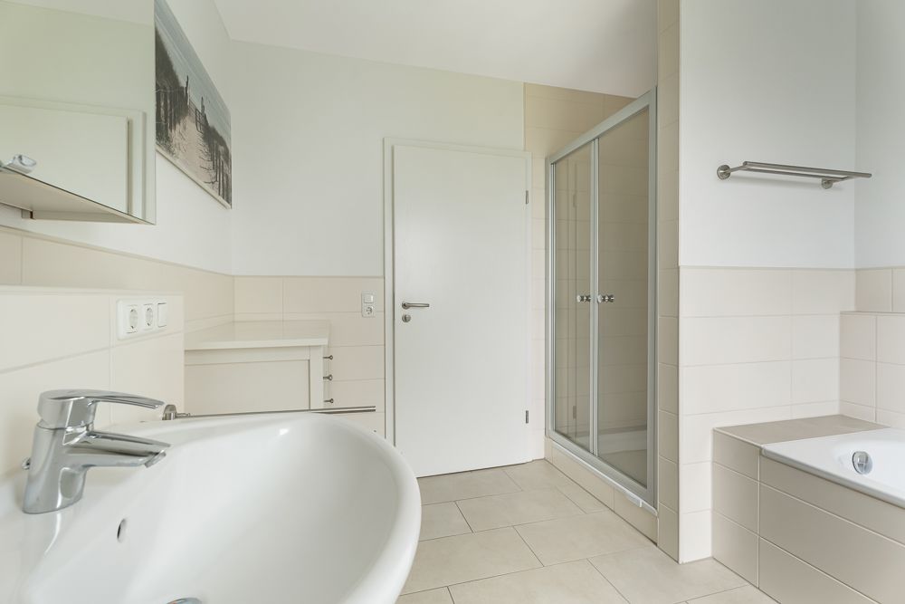 Helles Badezimmer mit Waschbecken, Dusche, Badewanne und weißer Tür.