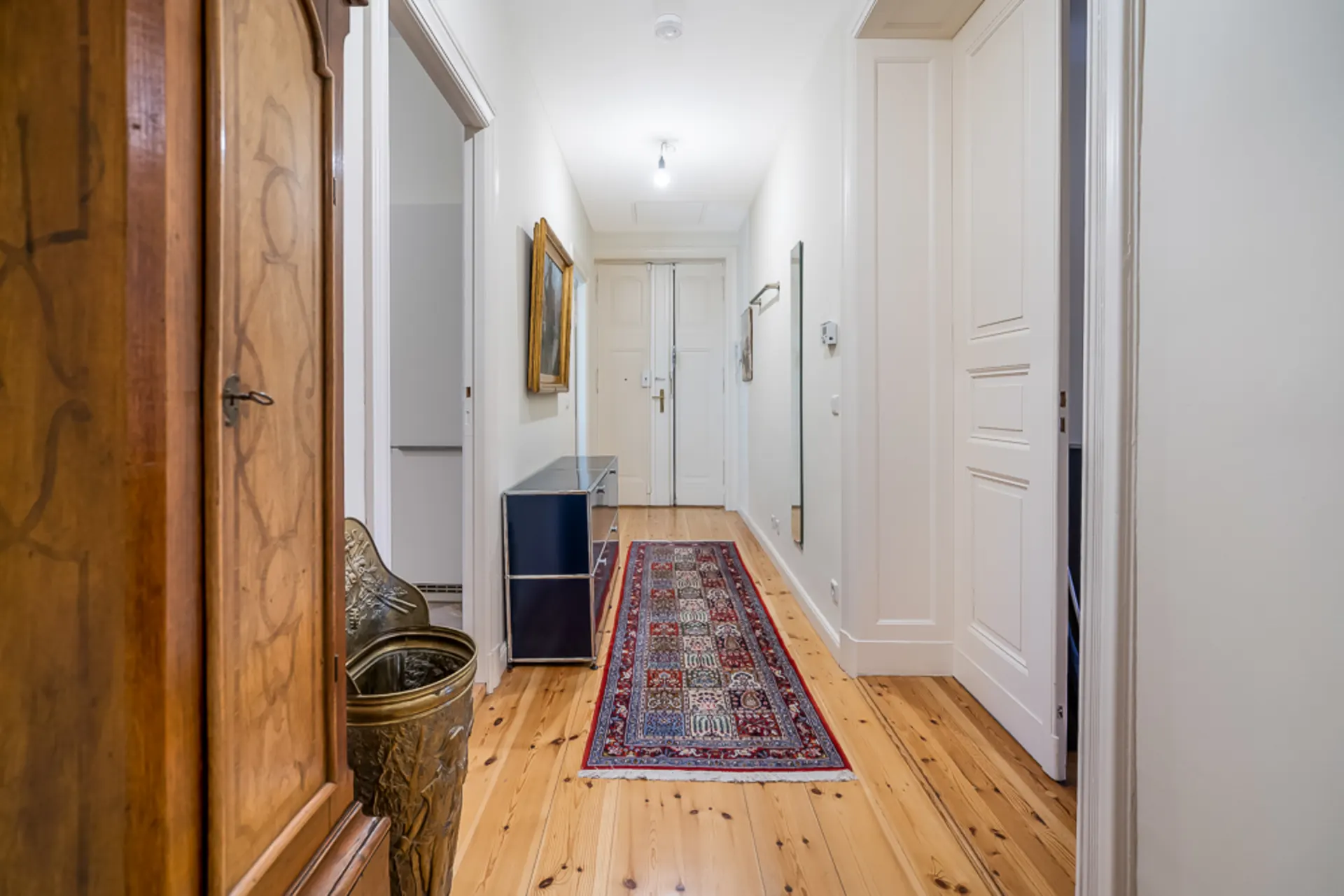 Heller Flur mit Holzboden, Teppichläufer, Kommode und Wandspiegel in einer Wohnung.