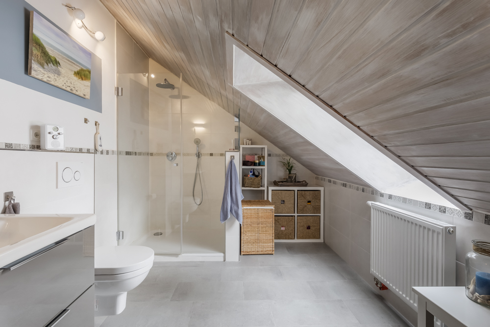 Modernes Badezimmer mit Dachschräge, Dusche, WC, Waschbecken und Regalen.