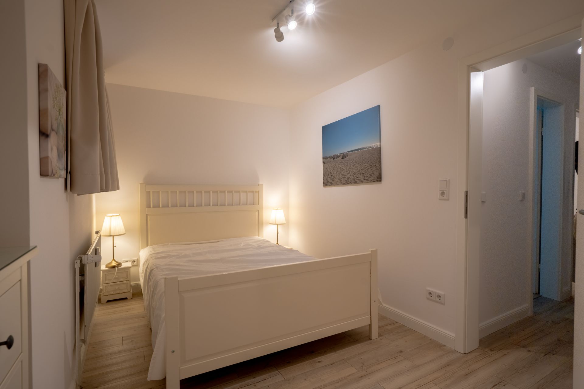 Schlafzimmer mit weißem Bett, zwei Nachttischen mit Lampen und Bild an der Wand.
