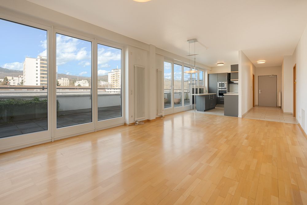 Helles Wohnzimmer mit Holzboden, großen Fenstern und offener Küche in einer Wohnung.