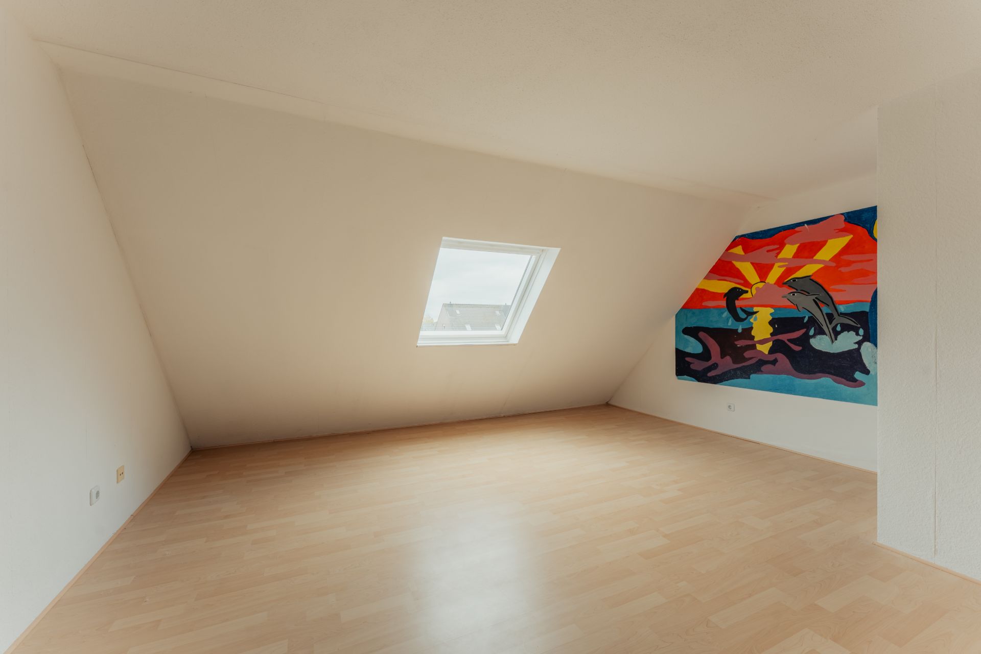 Helles Zimmer mit schräger Decke, Fenster und bunter Wandmalerei mit Delfinmotiv.