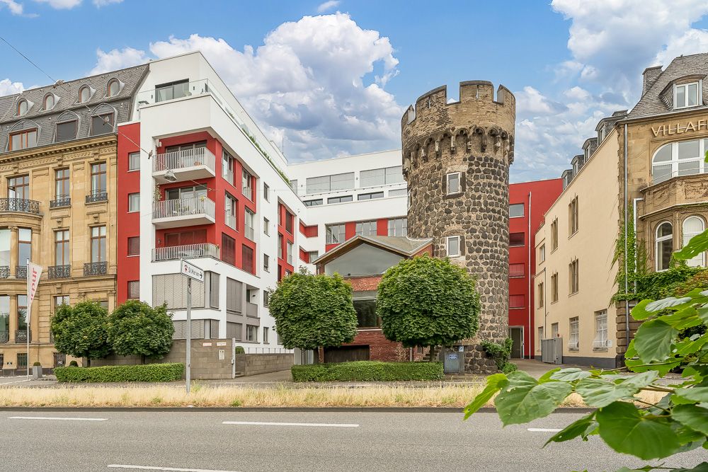 Wohngebäude mit modernen und historischen Fassaden sowie einem alten Steinturm und Bäumen davor.