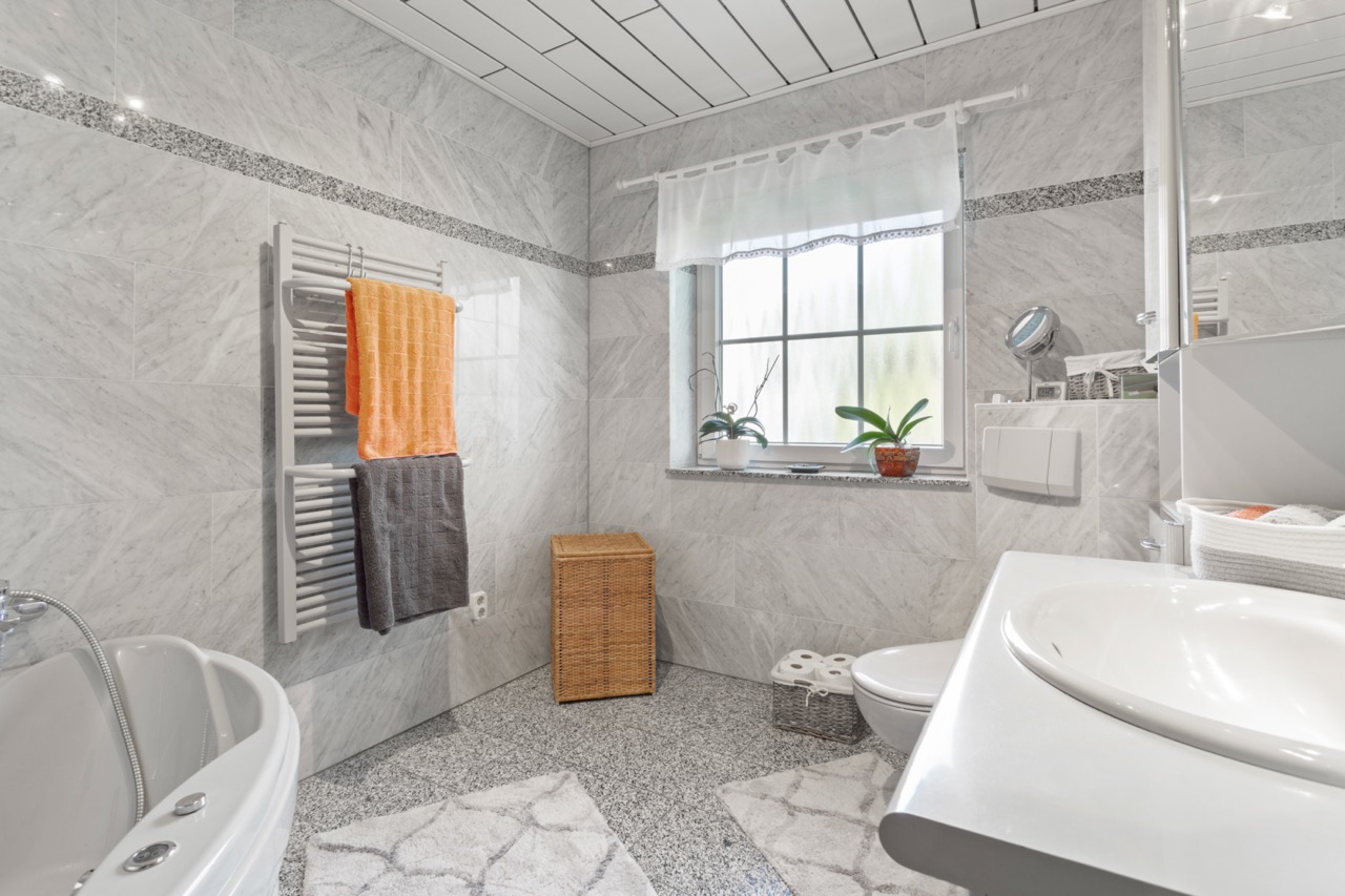 Helles Badezimmer mit Waschbecken, Badewanne, Handtuchhalter, Fenster und Pflanzen.