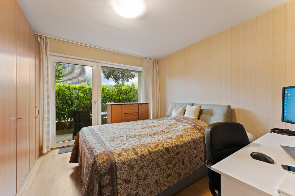 Helles Schlafzimmer mit Doppelbett, Schreibtisch, Kleiderschrank und Zugang zur Terrasse.
