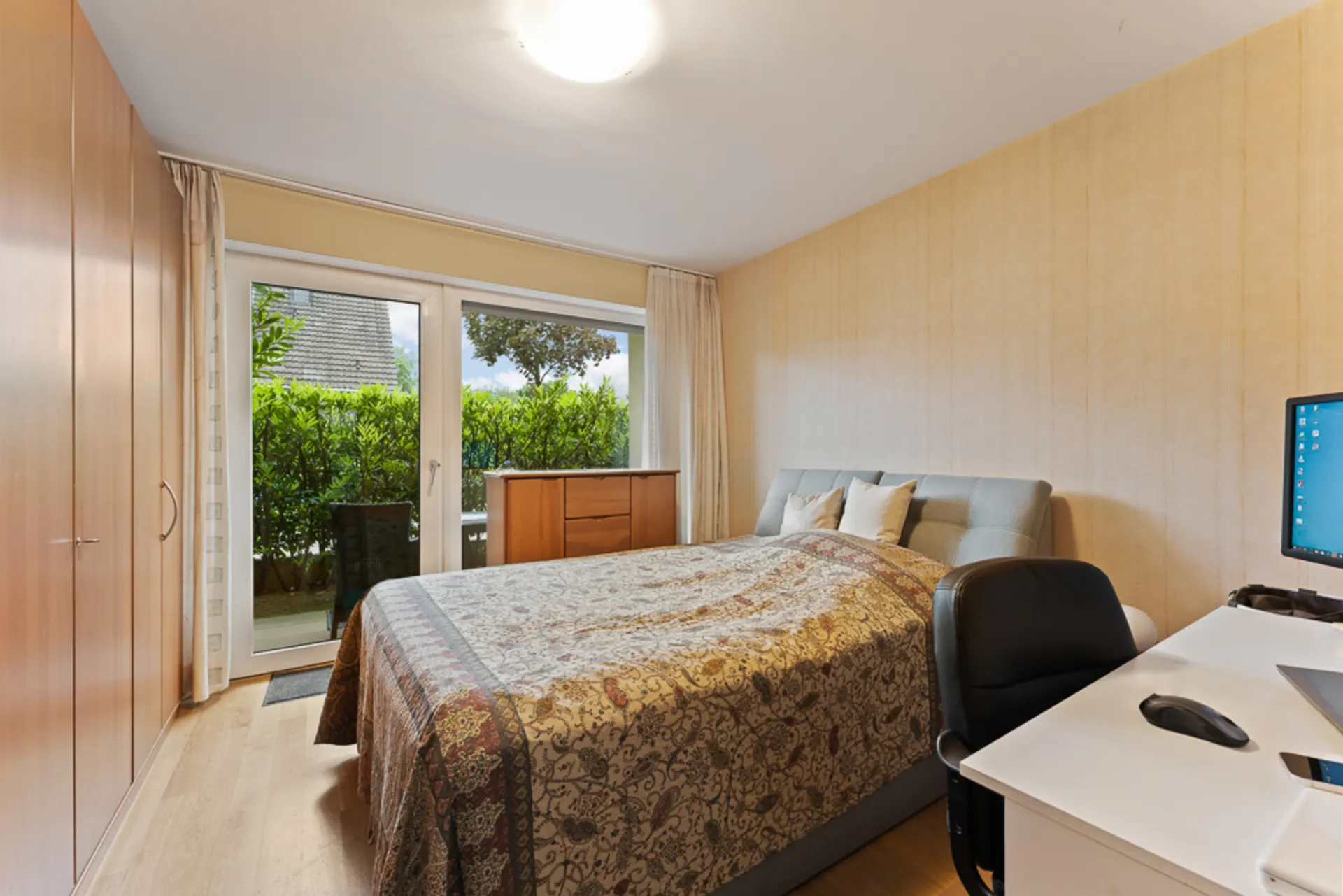 Helles Schlafzimmer mit Doppelbett, Schreibtisch, Kleiderschrank und Zugang zur Terrasse.