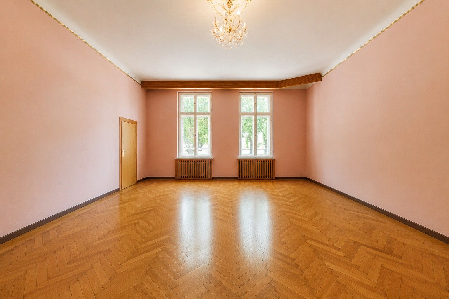 Leerer Raum mit rosa Wänden, Holzboden, zwei Fenstern, Tür und Kronleuchter.