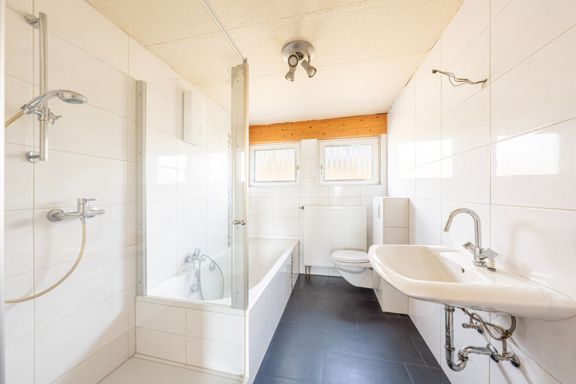 Helles Badezimmer mit Badewanne, Dusche, Waschbecken und WC, zwei kleine Fenster an der Rückwand.