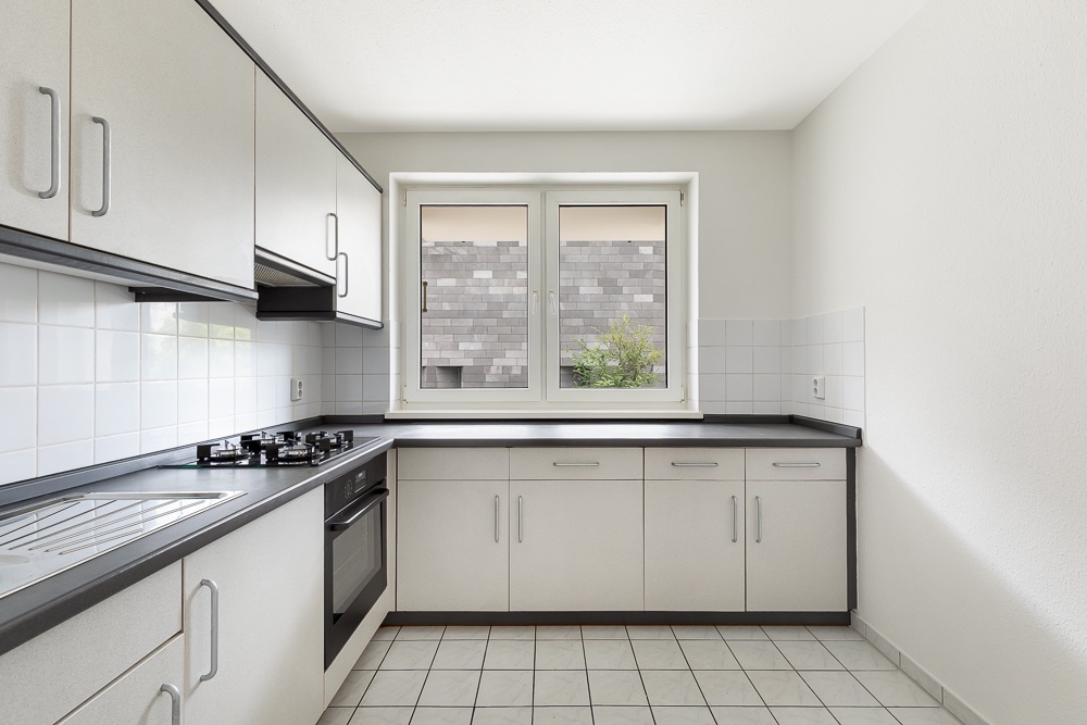 Helle, moderne Einbauküche mit weißen Schränken, Gasherd, Backofen und Fenster.