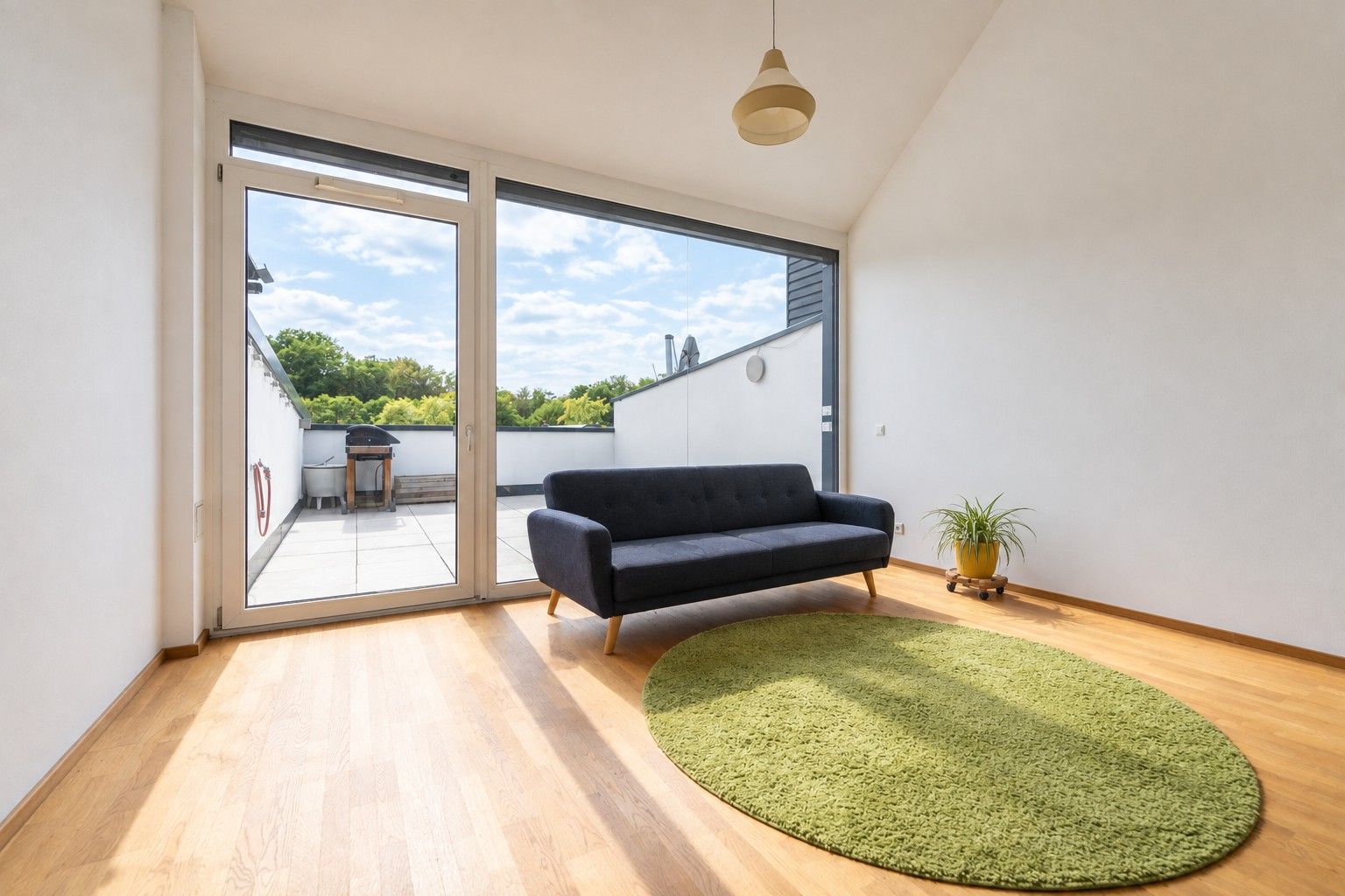 Helles Wohnzimmer mit Sofa, rundem Teppich und Zugang zur Terrasse mit Grill.
