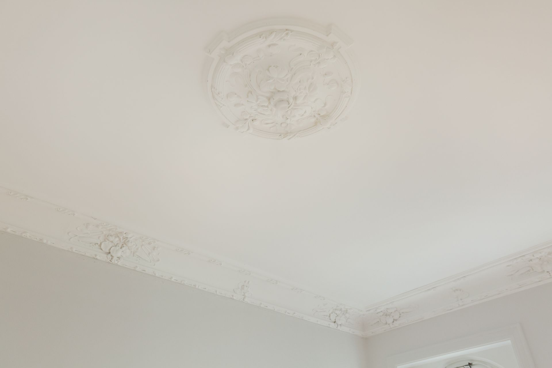 Weiße Decke mit Stuckverzierung und Zierleiste in einem Raum.
