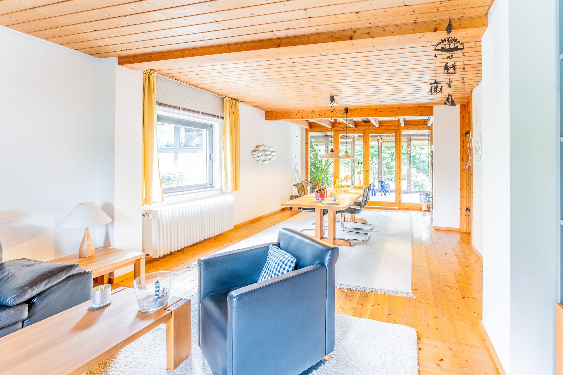 Helles Wohnzimmer mit Holzdecke, Esstisch, großen Fenstern und modernen Möbeln.