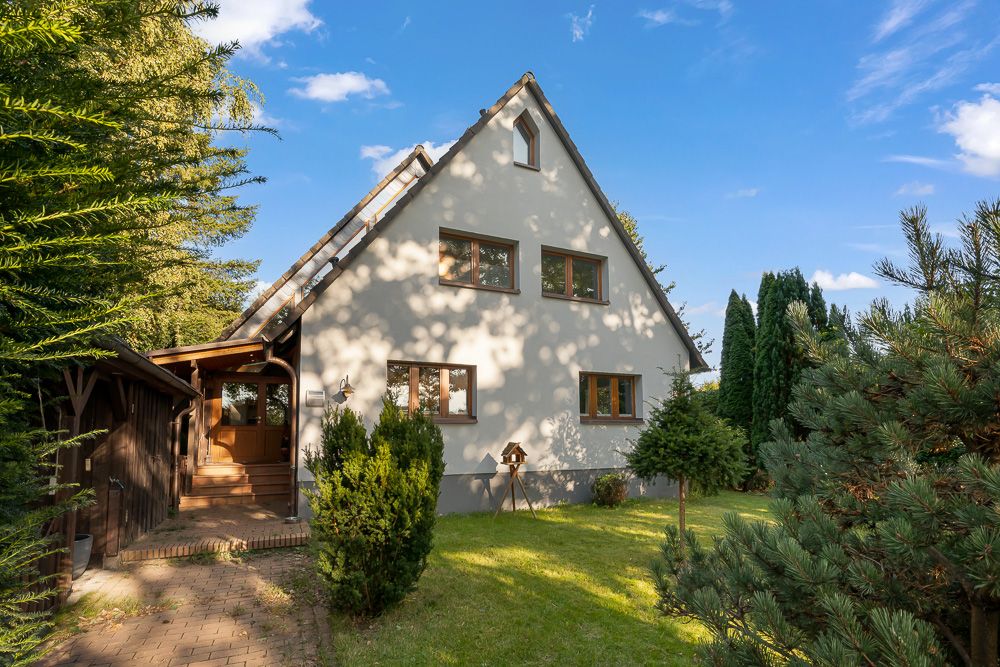 Einfamilienhaus mit Satteldach, Vorgarten und Bäumen bei sonnigem Wetter.