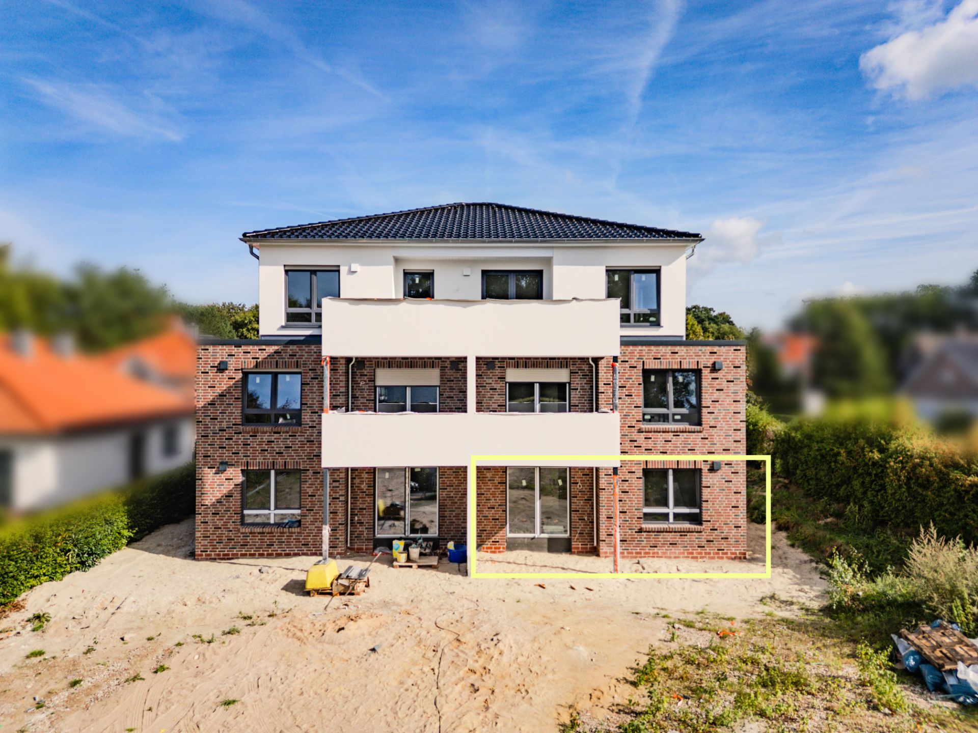 Zweistöckiges Wohngebäude aus Klinker mit Balkonen und großen Fenstern, Baustelle im Vordergrund.