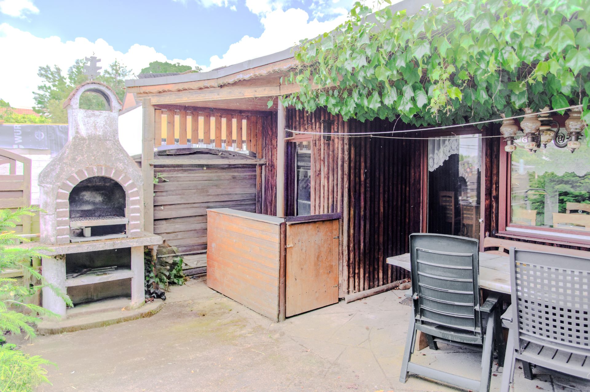 Gartenbereich mit gemauertem Grill, Holzzaun und Sitzgruppe auf einer Terrasse.