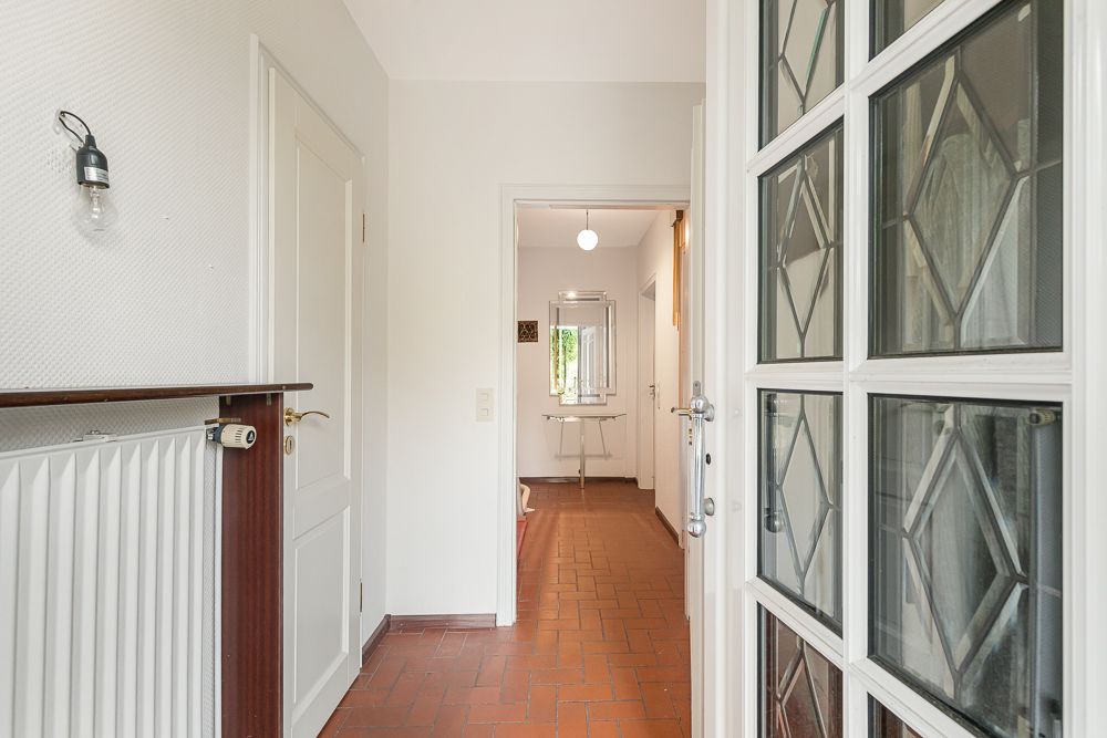 Heller Flur mit Glastür, Heizkörper und Blick auf einen Spiegel an der Wand.
