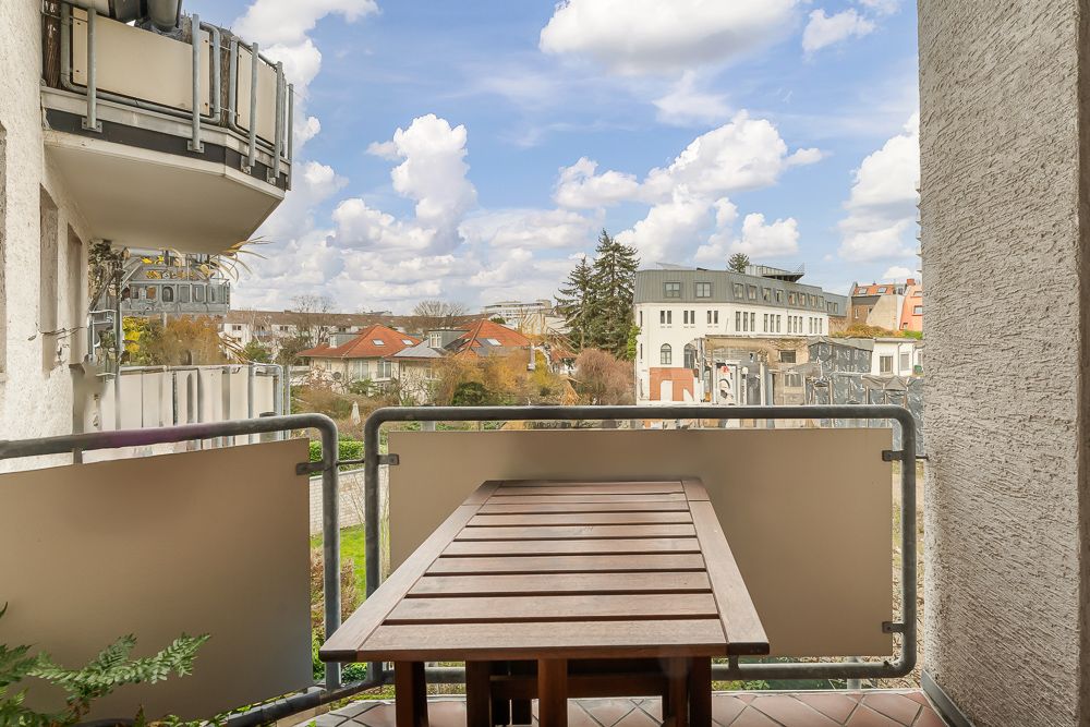 Holztisch steht auf einem Balkon mit Blick auf Nachbarhäuser und einen Garten.