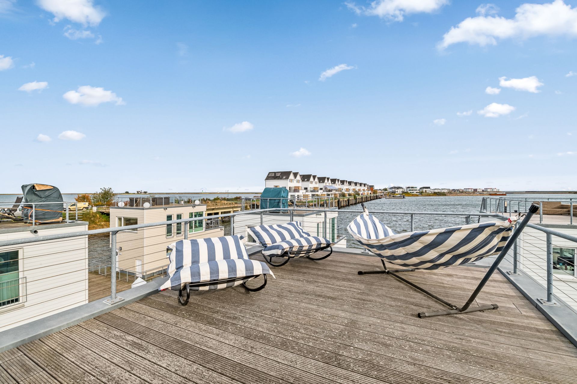 Große Terrasse mit Liegestühlen und Hängematte, Blick auf Wasser und benachbarte Gebäude.