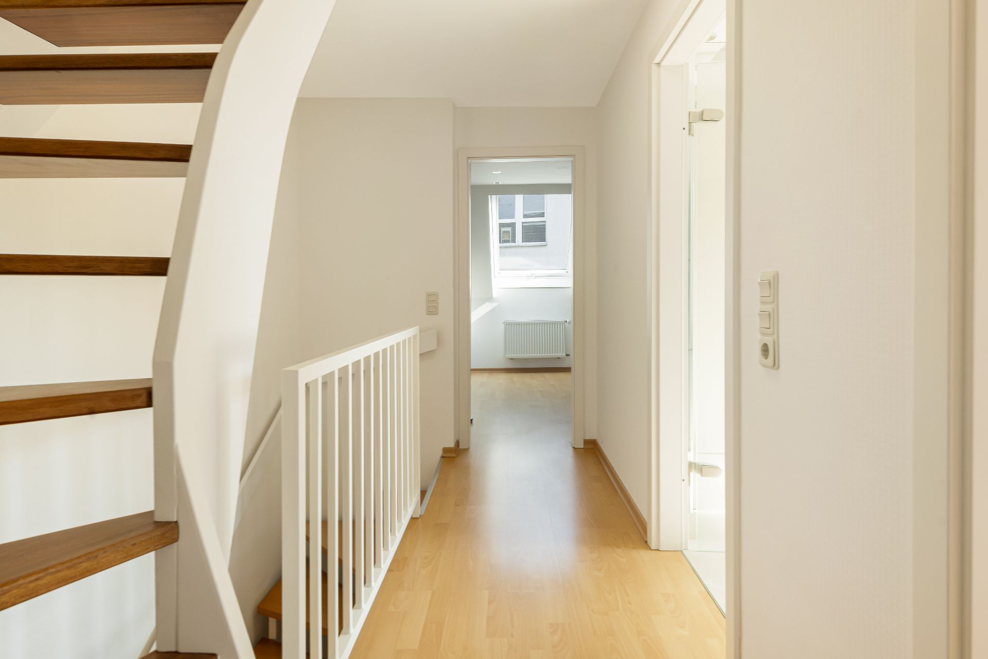 Heller Flur mit Holztreppe, hellen Wänden und Blick in ein weiteres Zimmer.
