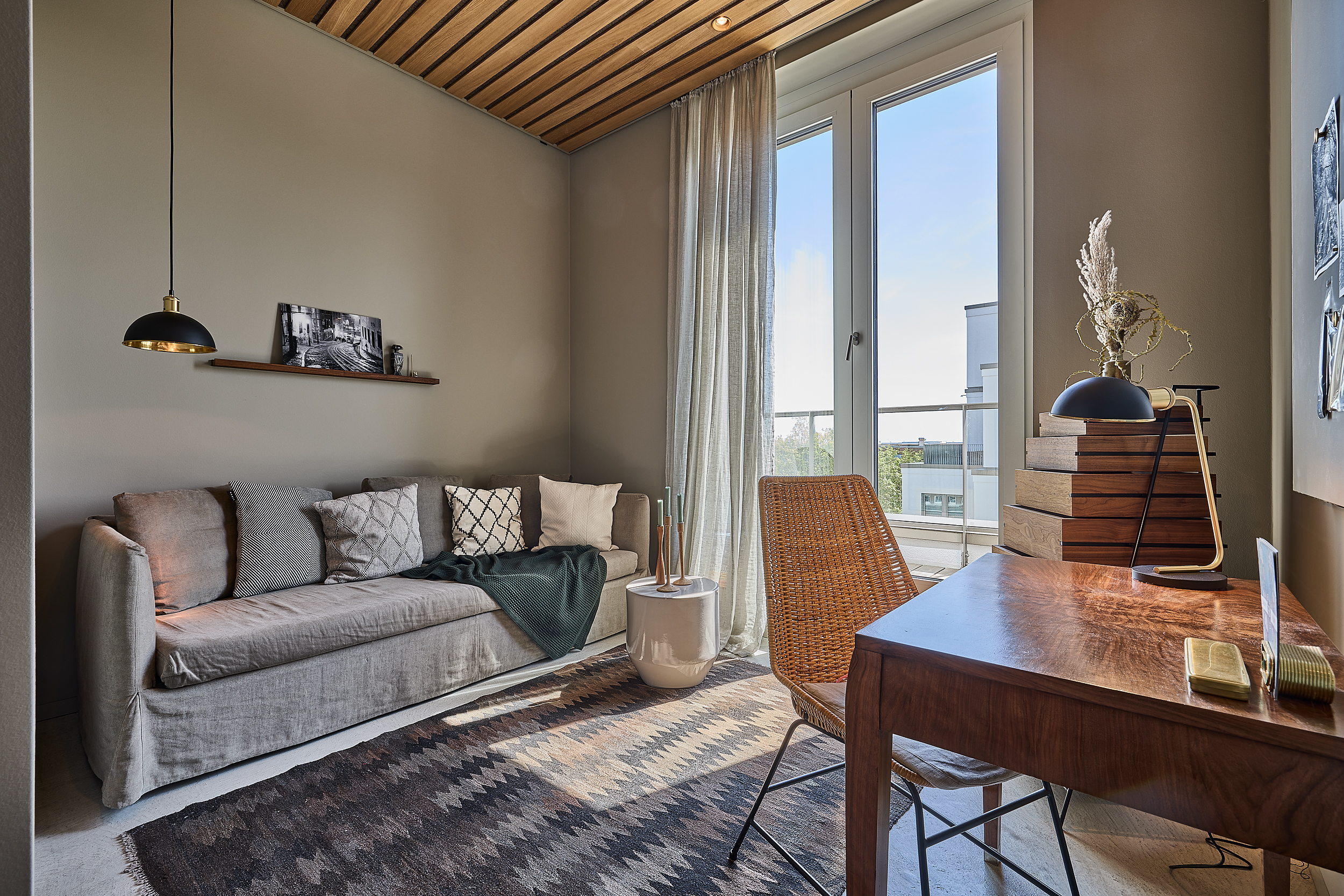 Helles Wohnzimmer mit Sofa, Holztisch, Stuhl, Teppich und großen Fenstern.