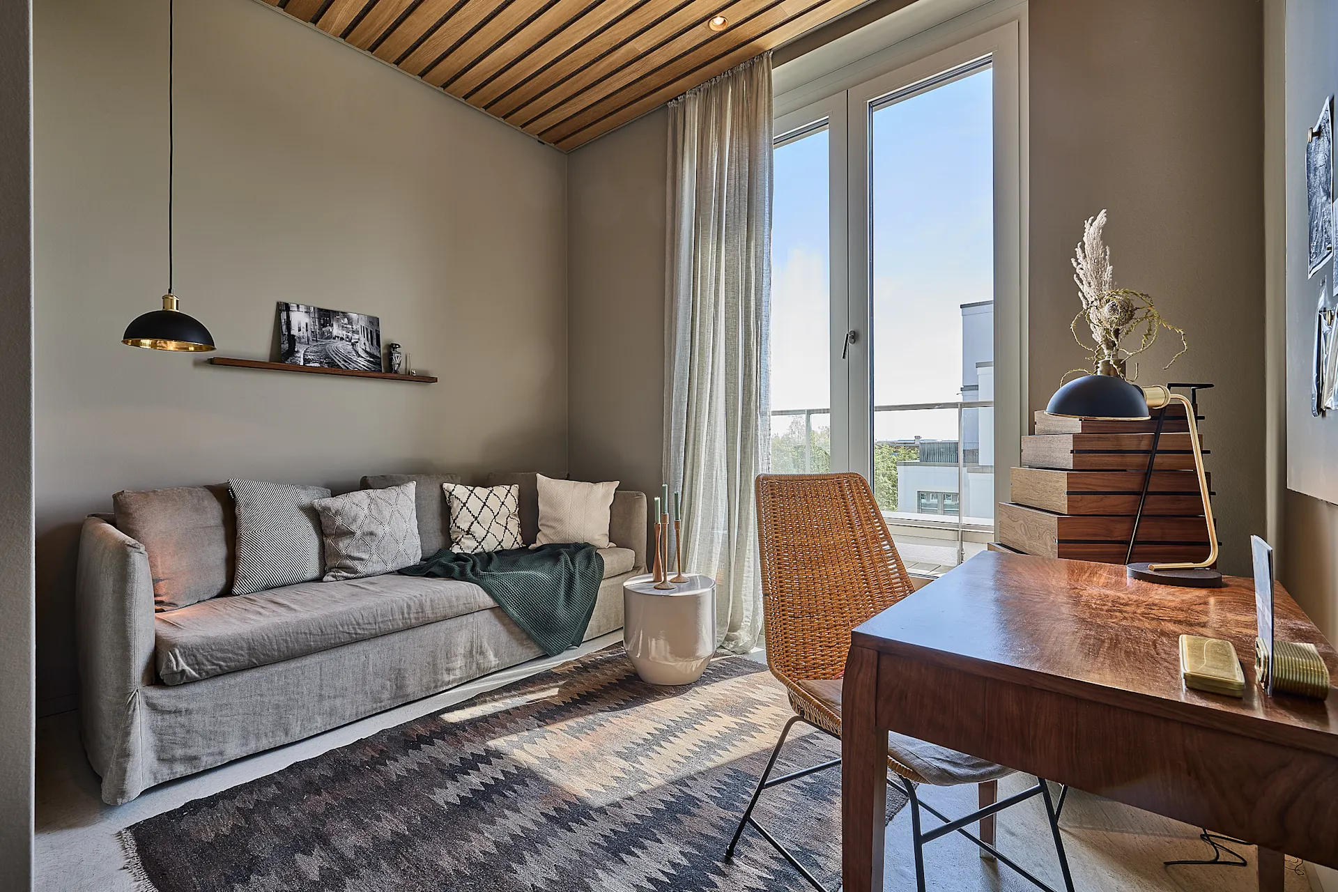 Helles Wohnzimmer mit Sofa, Holztisch, Stuhl, Teppich und großen Fenstern.