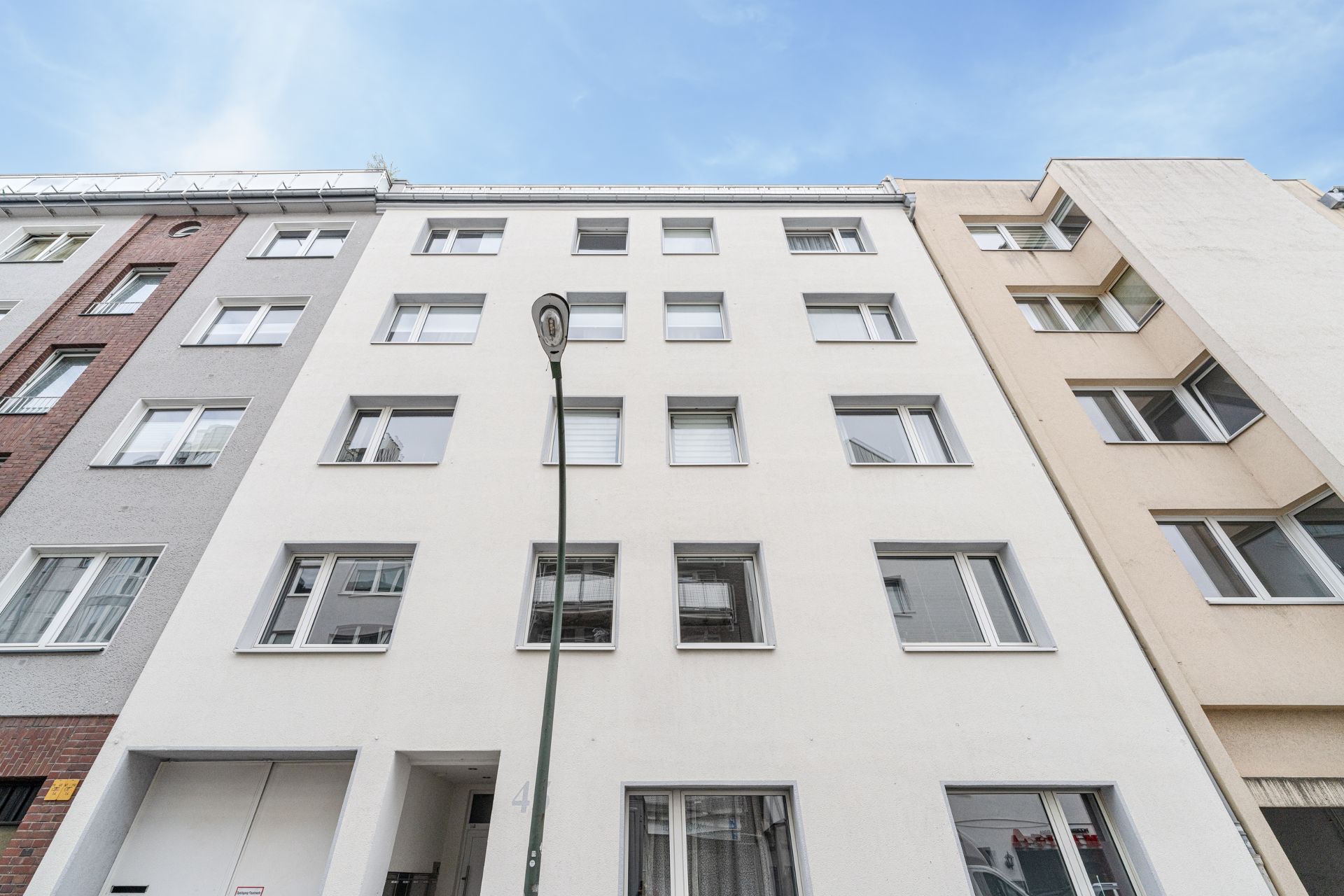 Fünfstöckiges Wohnhaus mit heller Fassade und vielen Fenstern, gesehen von unten.