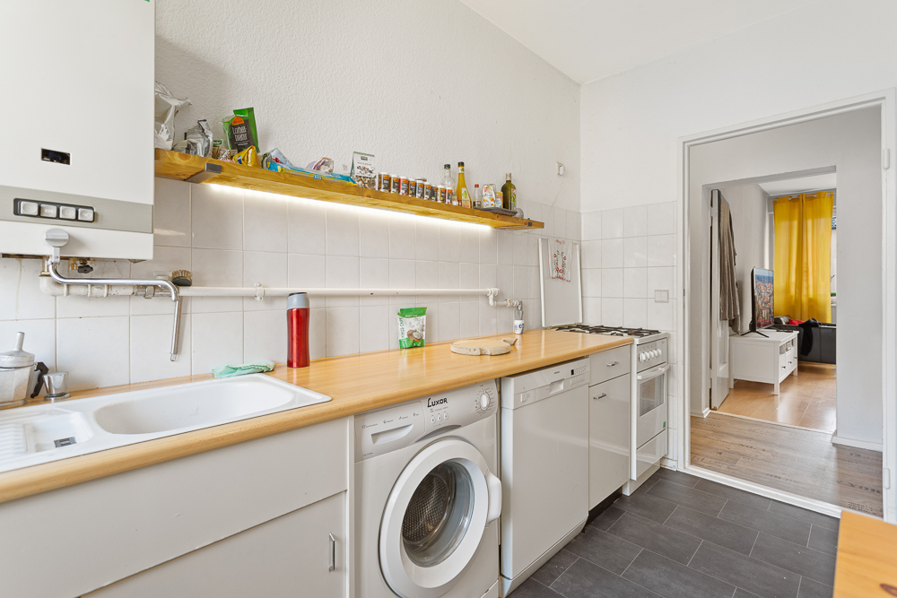 Helle Küche mit Waschmaschine, Spülmaschine, Herd und Holzarbeitsplatte, Durchgang zum Wohnzimmer.