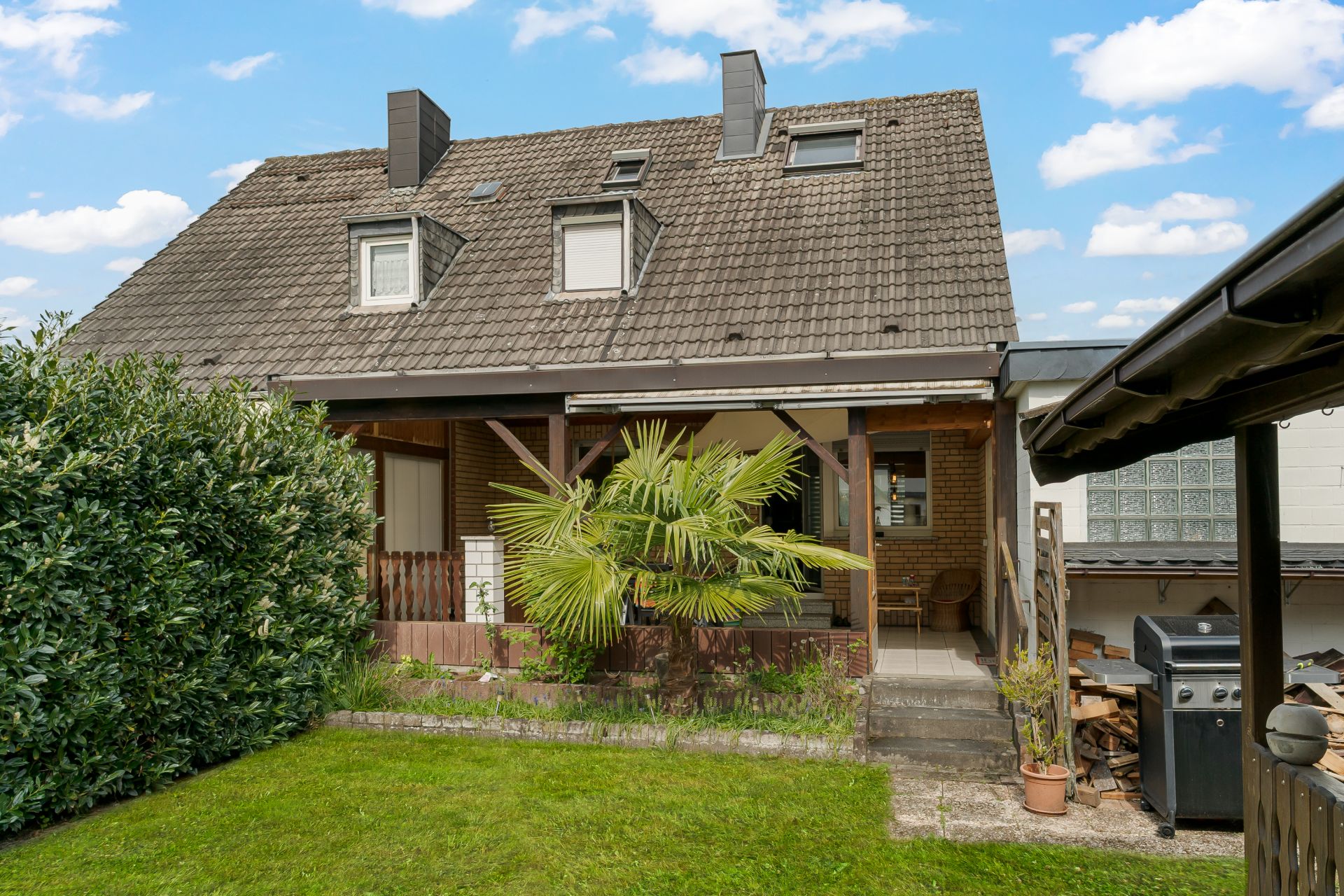 Rückansicht eines Hauses mit Terrasse, Garten, Palmenpflanze und Grill.