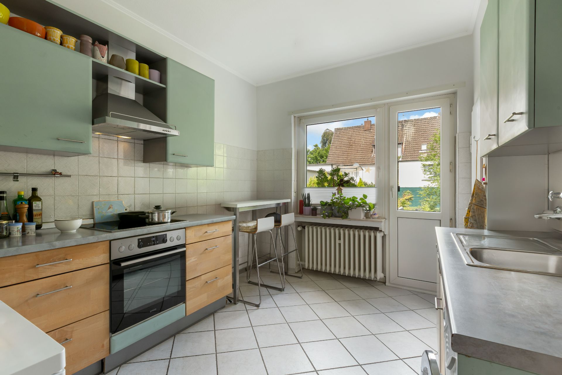 Helle Küche mit Esstisch, Herd, Spüle und Blick auf den Garten durch ein Fenster.