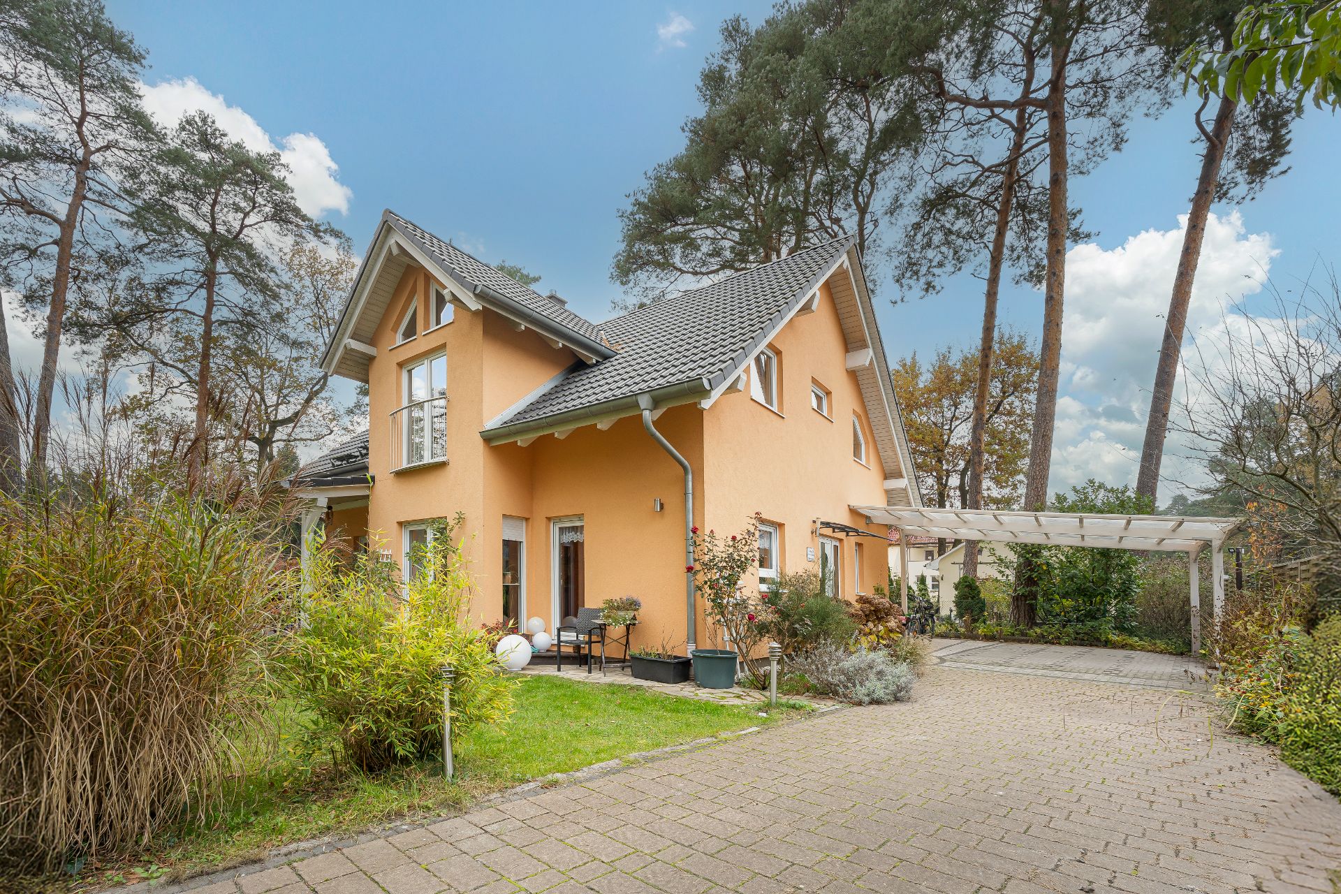 Zweistöckiges gelbes Haus mit Garten, Terrasse und einem Carport, umgeben von Bäumen.