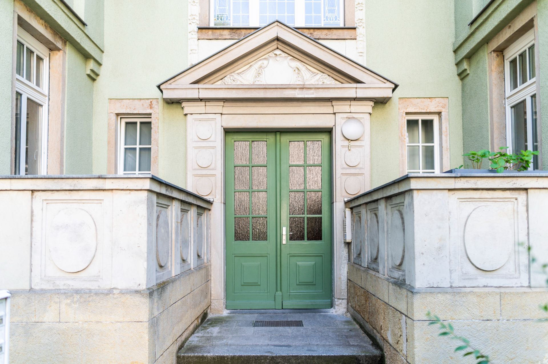 Grüne Eingangstür mit Glasfenstern, von Steinmauern und Fenstern umgeben.