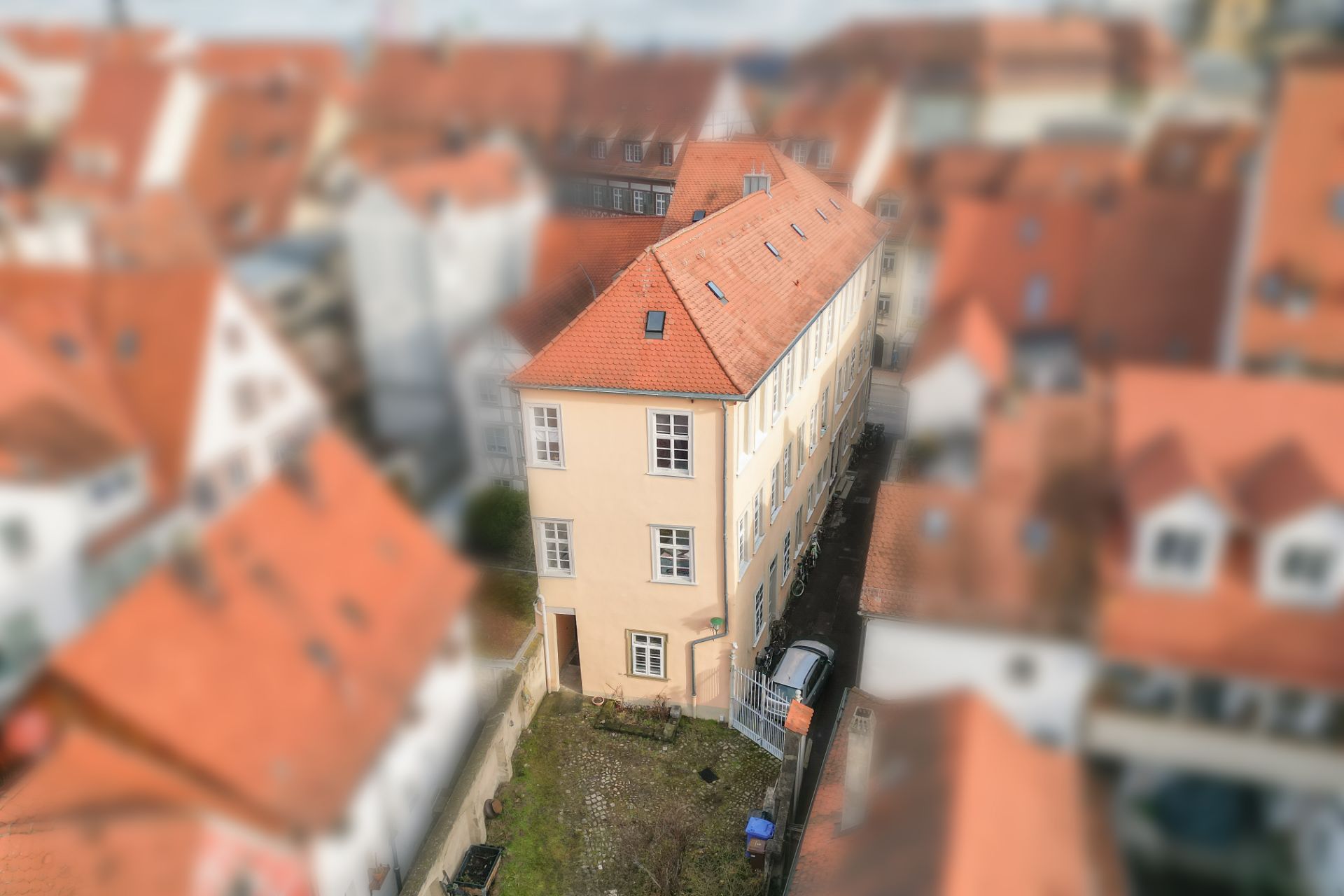 Beiges Wohnhaus mit rotem Dach und Garten, umgeben von weiteren Häusern mit roten Dächern.