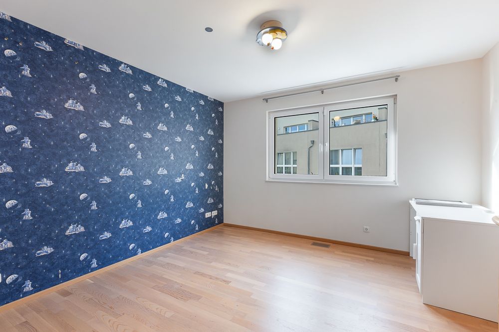 Helles Zimmer mit Holzboden, blauer Motivtapete und zwei Fenstern.