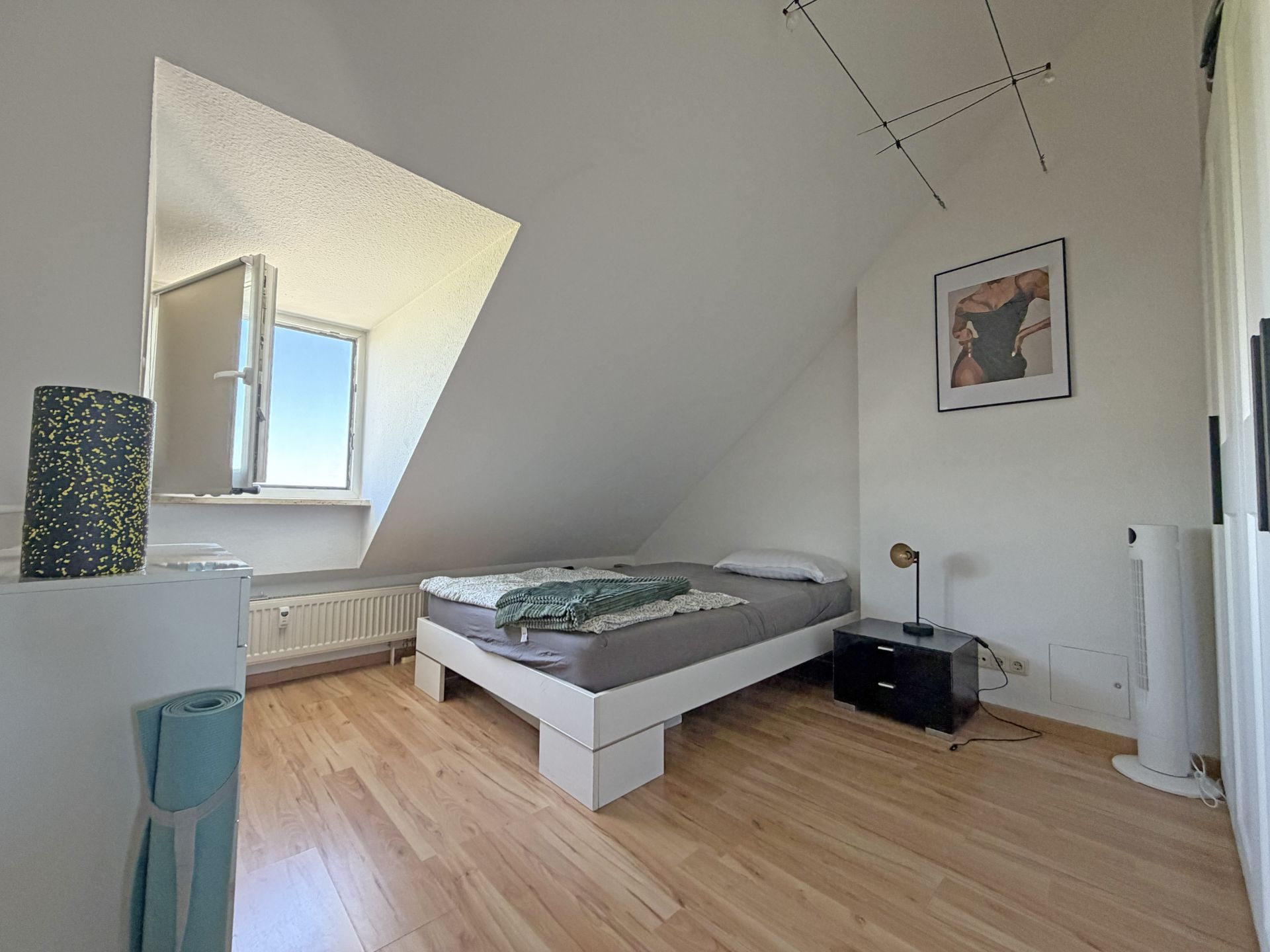 Helles Schlafzimmer mit Einzelbett, offenem Fenster und schräger Decke.