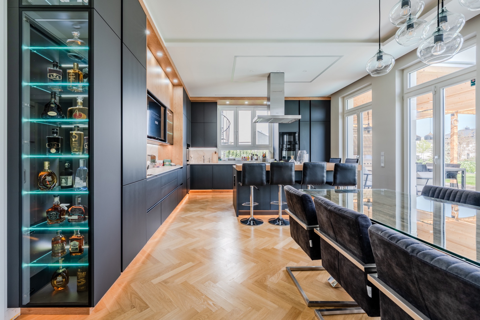 Moderne Küche mit Glastisch, schwarzen Stühlen und beleuchtetem Regal mit Getränkeflaschen.