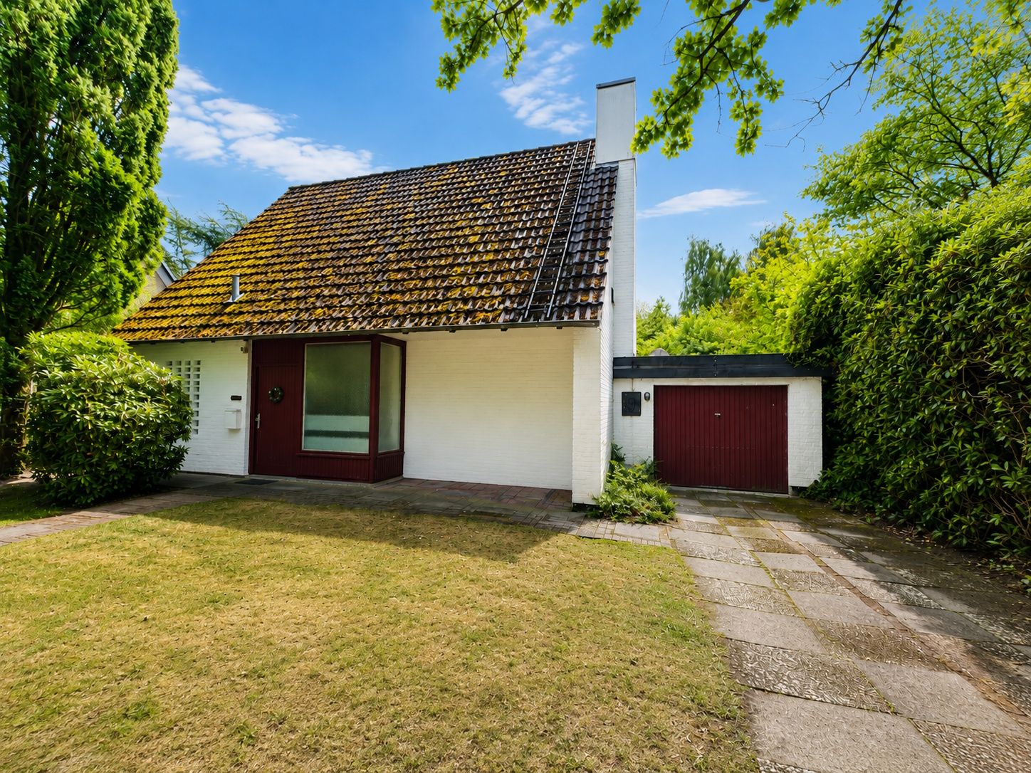 Einfamilienhaus mit schrägem Dach, Garage und Vorgarten an einem sonnigen Tag.