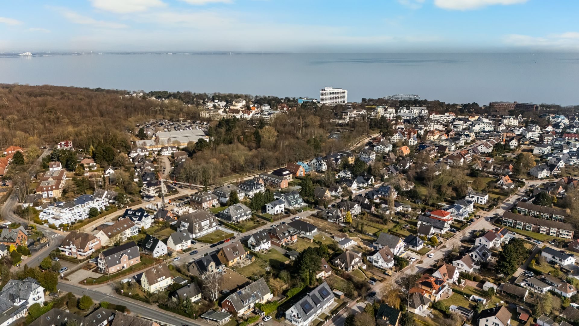 Luftaufnahme eines Wohngebiets mit vielen freistehenden Häusern und Bäumen am Wasser.