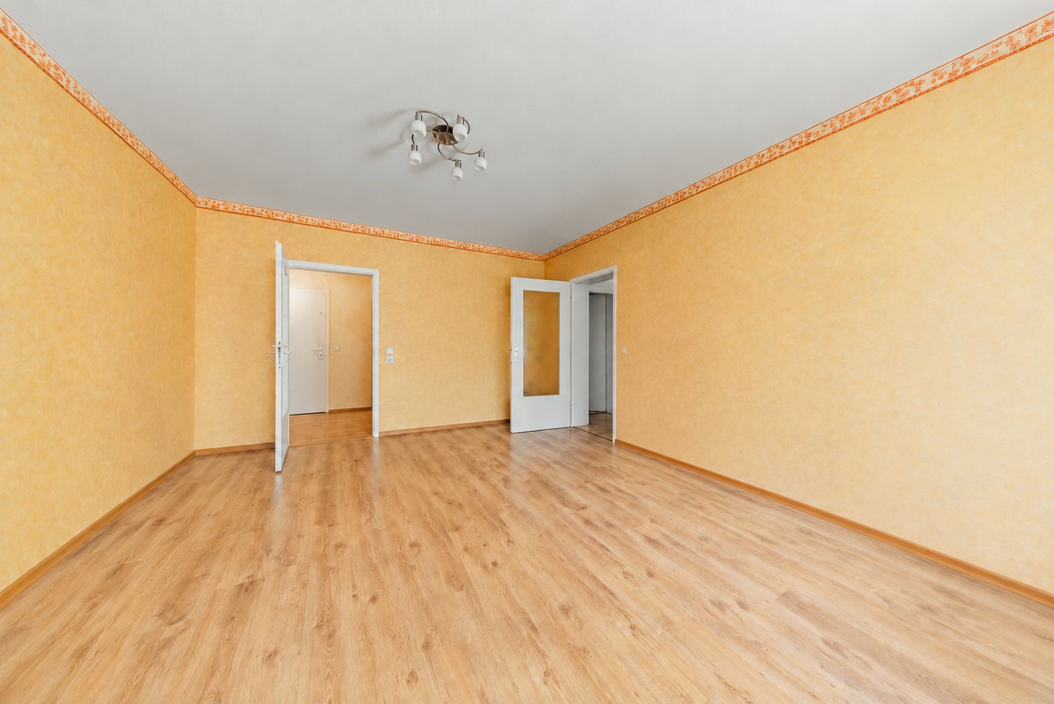 Leerer Raum mit gelben Wänden, Holzfußboden und zwei offenen weißen Türen.