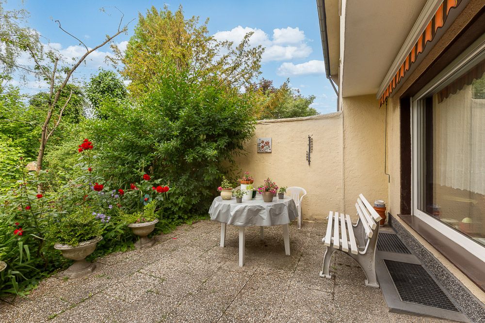 Gepflasterte Terrasse mit Tisch, Stühlen, Bank und vielen Pflanzen im Grünen.