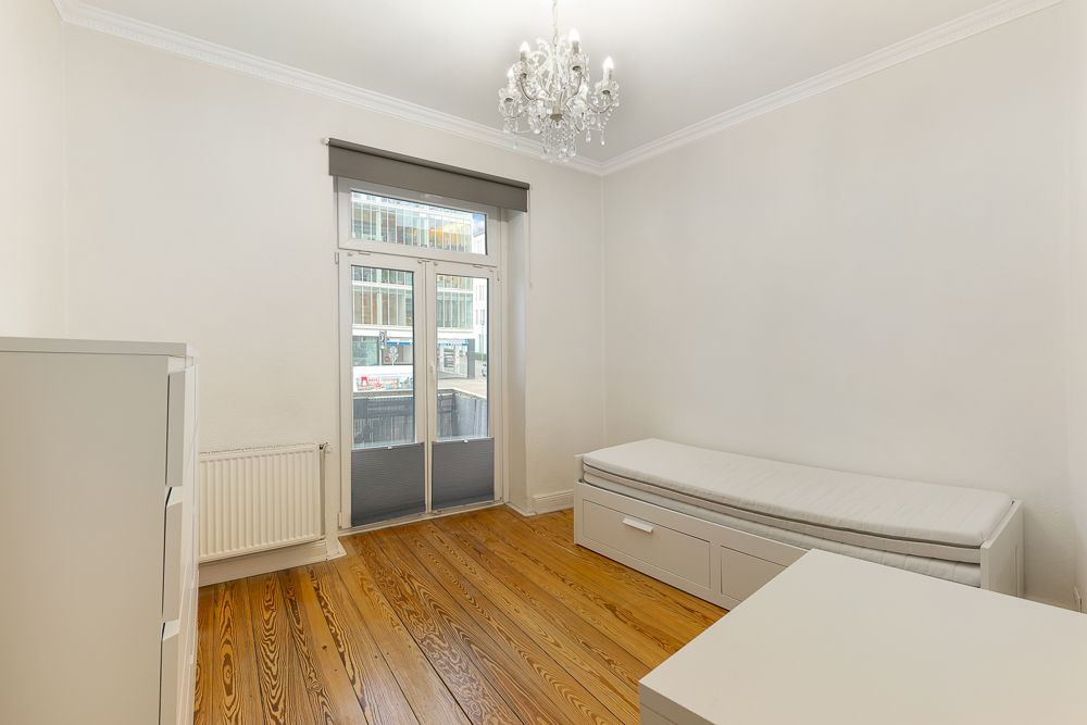 Helles Zimmer mit Holzboden, Einzelbett, Kommode, Fenster und Kronleuchter.