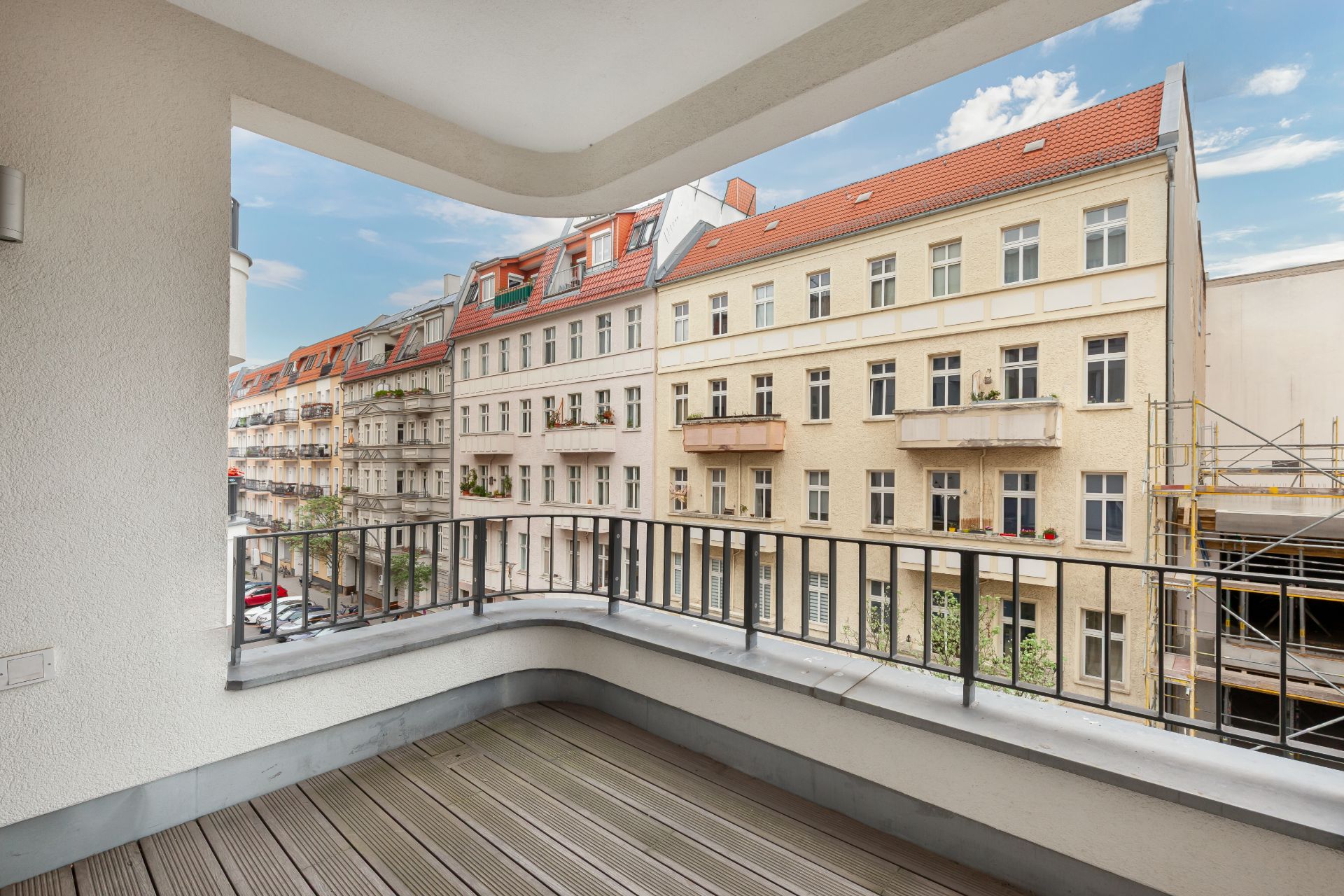 Überdachter Balkon mit Holzboden und Blick auf Nachbargebäude mit Balkonen.
