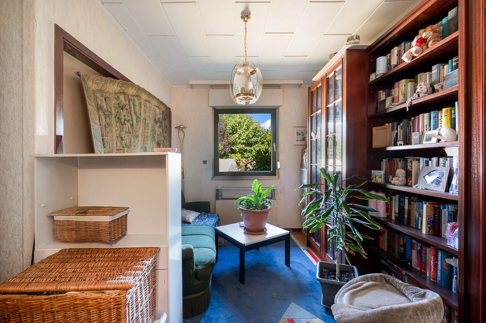 Kleines Wohnzimmer mit Sofa, Couchtisch, Bücherregal, Pflanzen und Fenster mit Blick ins Grüne.