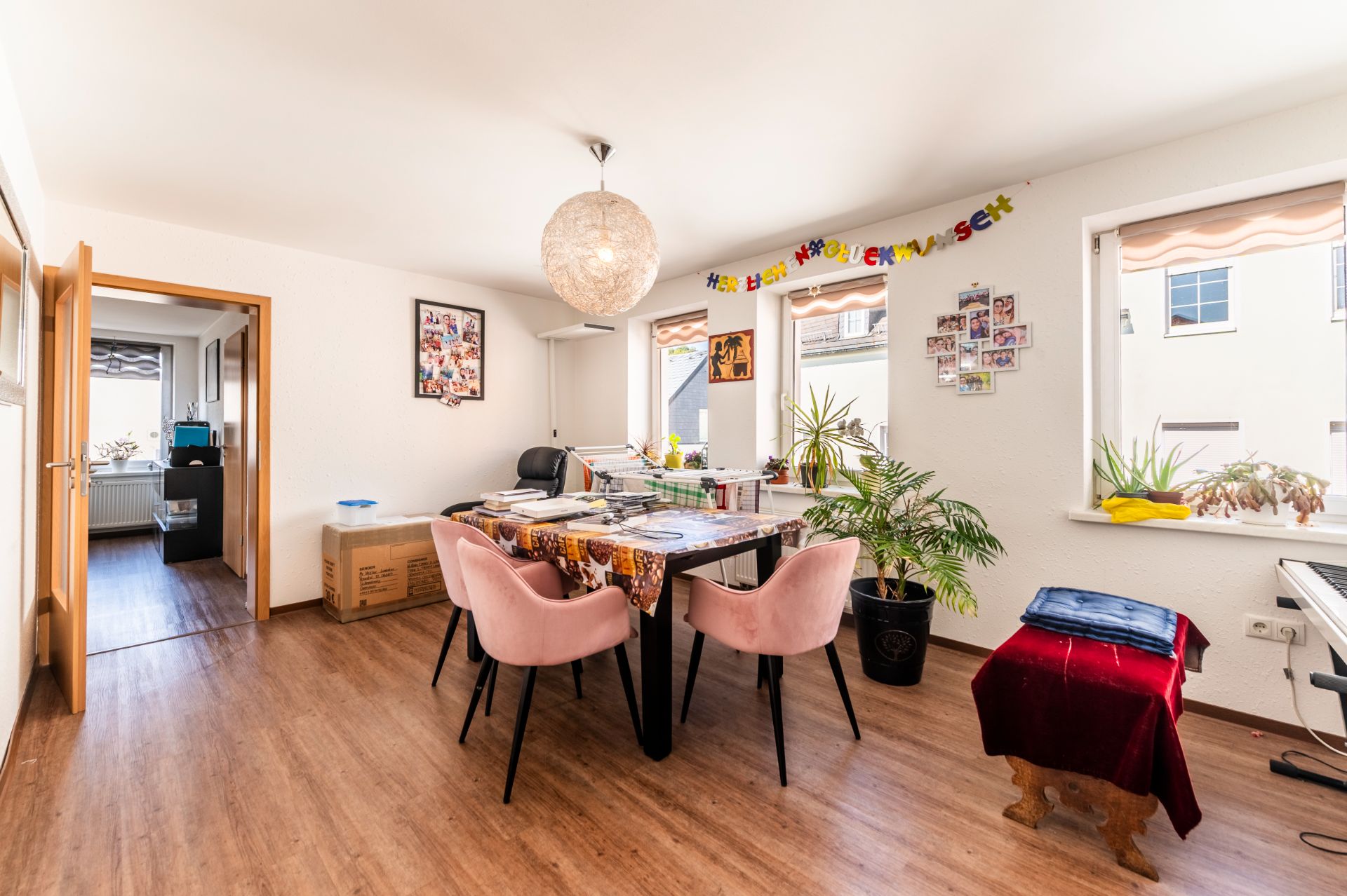 Helles Esszimmer mit Tisch, rosa Stühlen, Pflanzen und Dekoration an den Wänden.