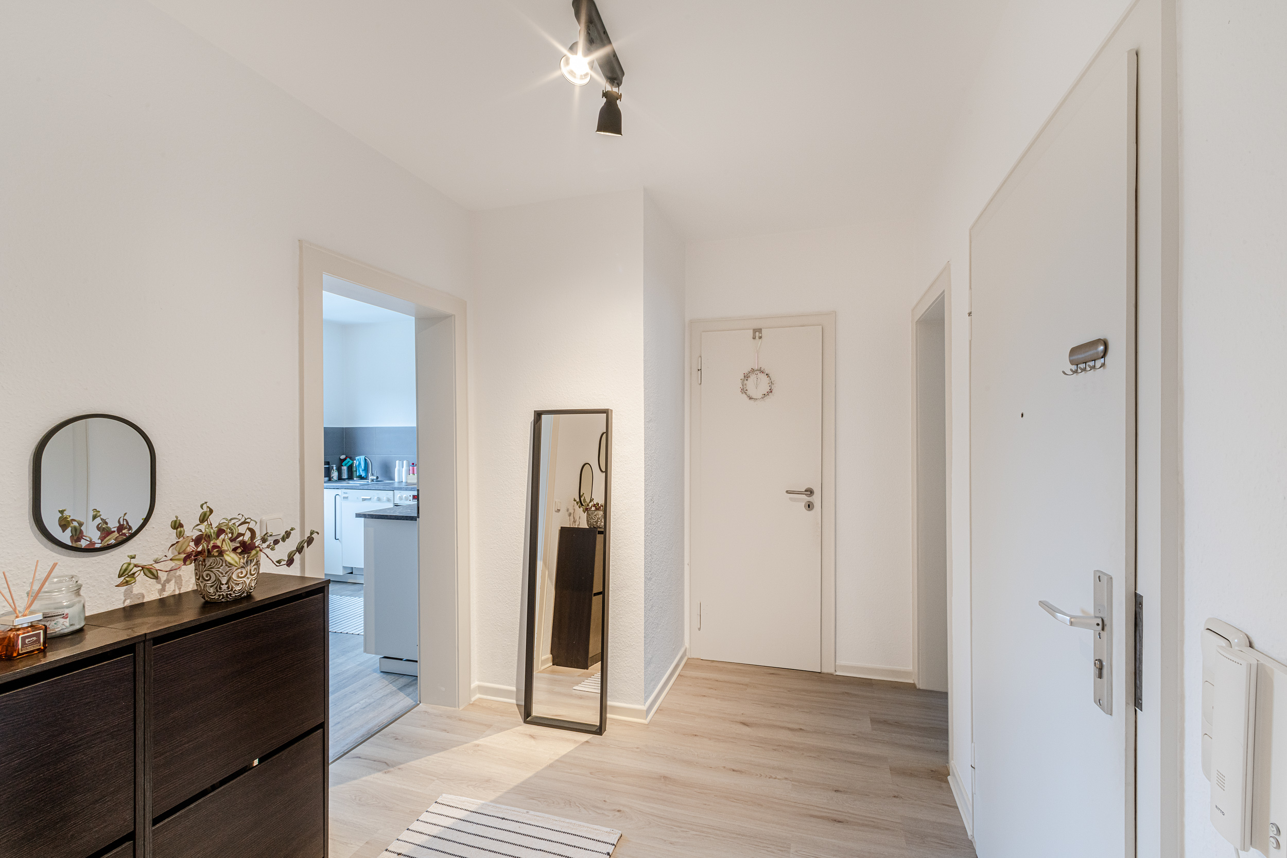 Heller Flur mit Spiegel, Kommode, Pflanze und Blick in eine weiße Küche.