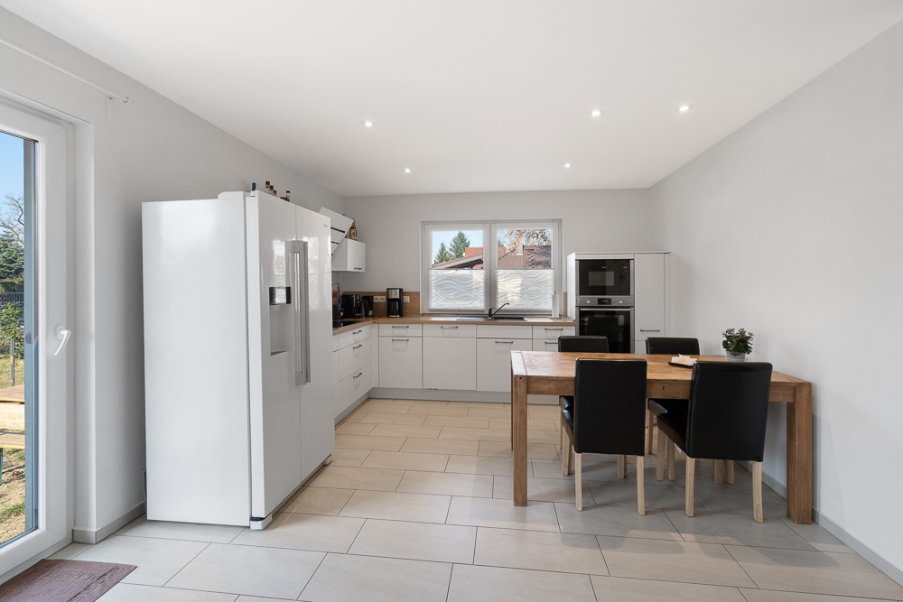 Moderne Küche mit großem Kühlschrank, Esstisch aus Holz und vier schwarzen Stühlen.